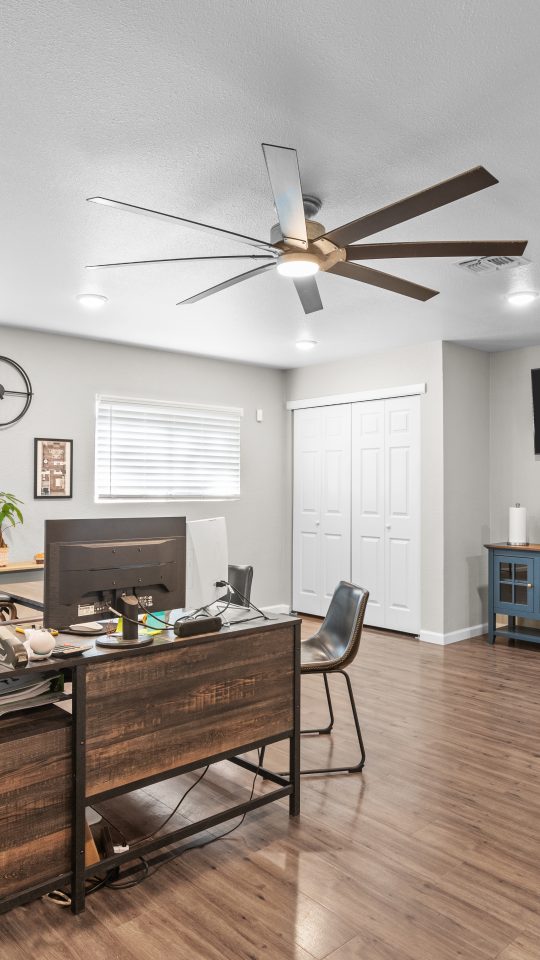a home office with a ceiling fan and hardwood floors at The Calypso Apartments